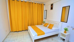 Ein Schlafzimmer mit einem Bett, Vorhängen, einem Nachttisch, einem Spiegel und einem kleinen Regal mit einer Vase.