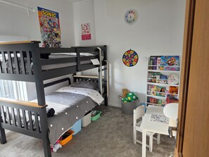 Un lit superposé avec des tiroirs de rangement, un bureau avec une chaise, une bibliothèque, une horloge murale et une affiche.