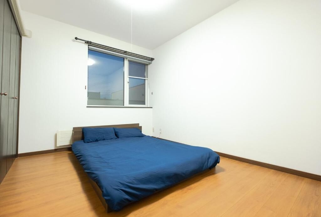 A bedroom with a single bed, a window with blinds, and a wooden floor.