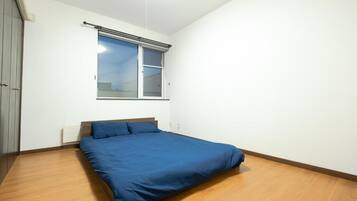 A bedroom with a single bed, a window with blinds, and a wooden floor.