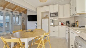 A modern kitchen with white cabinets, a wooden dining table, and a large window overlooking a scenic view. - Apartment 'Emelia' with Sea View, Wi-Fi and Air Conditioning (Lixouri)