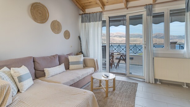 A room with a sofa, a small table, a view of the outdoors, and a ceiling with wooden beams. - Apartment 'Emelia' with Sea View, Wi-Fi and Air Conditioning (Lixouri)