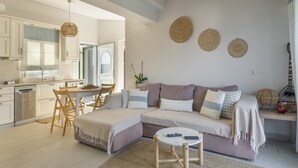 A modern kitchen with white cabinets, a dining area with a table and chairs, a large sofa with a throw blanket, and a hanging light fixture. - Apartment 'Emelia' with Sea View, Wi-Fi and Air Conditioning (Lixouri)