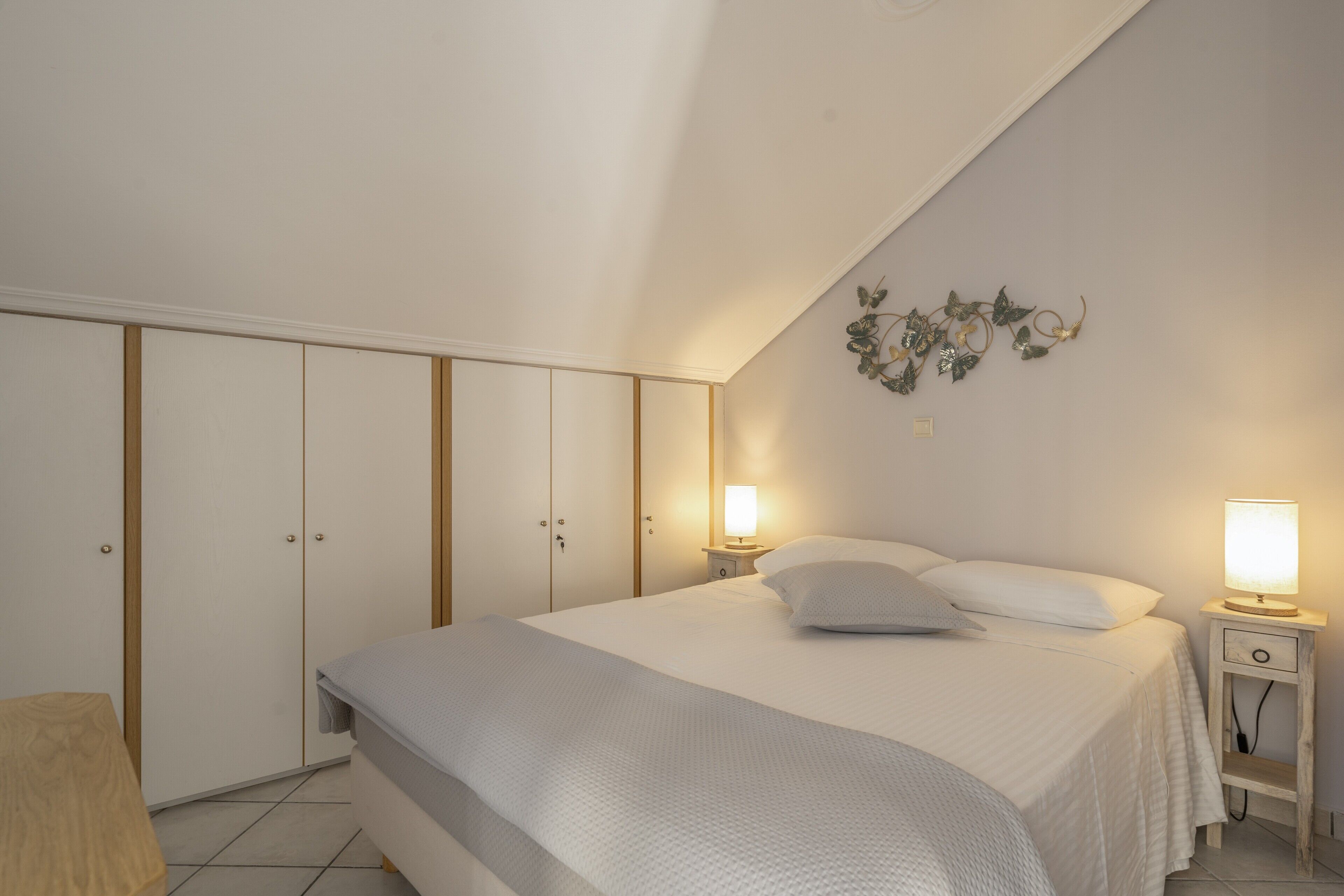 A bedroom with a bed, bedside lamps, a wardrobe, and a wall decoration.