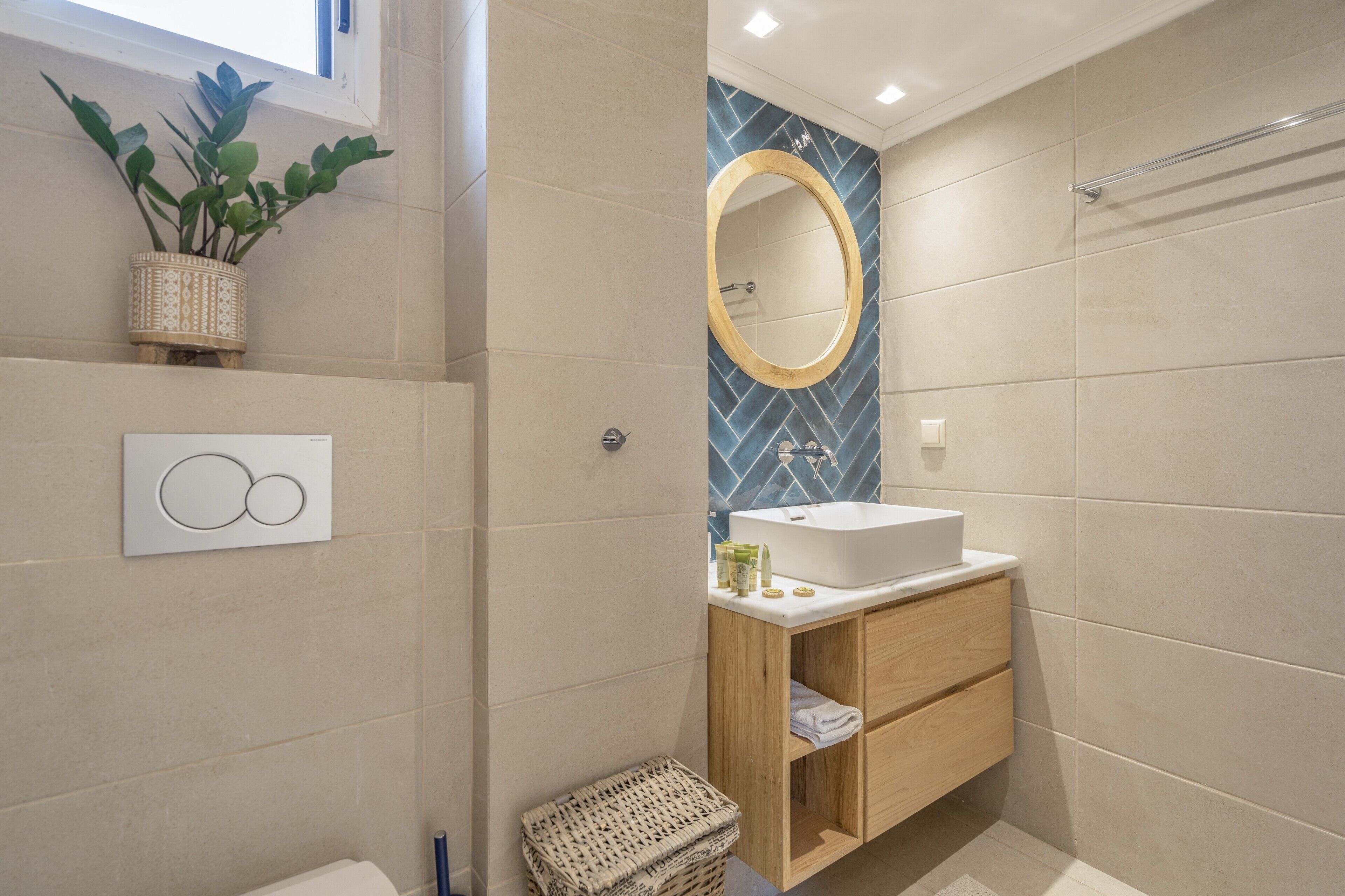 Un baño moderno con un lavamanos blanco, tocador de madera, un espejo y una planta en maceta.