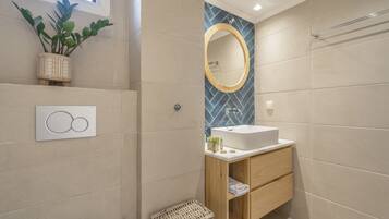 Un baño moderno con un lavamanos blanco, tocador de madera, un espejo y una planta en maceta.