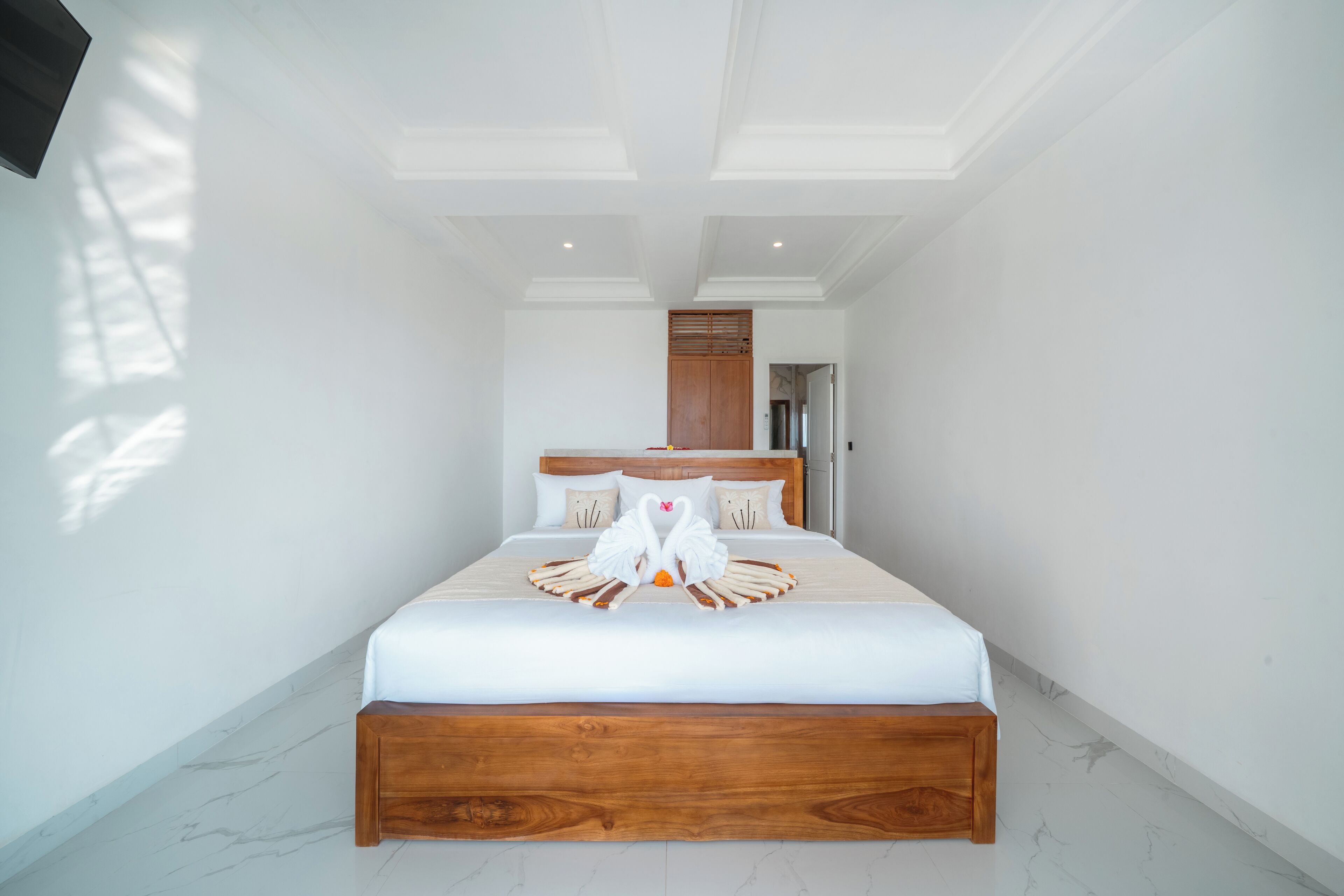 A spacious, well-lit bedroom with a large bed, wooden headboard, and a unique swan-shaped bedspread.