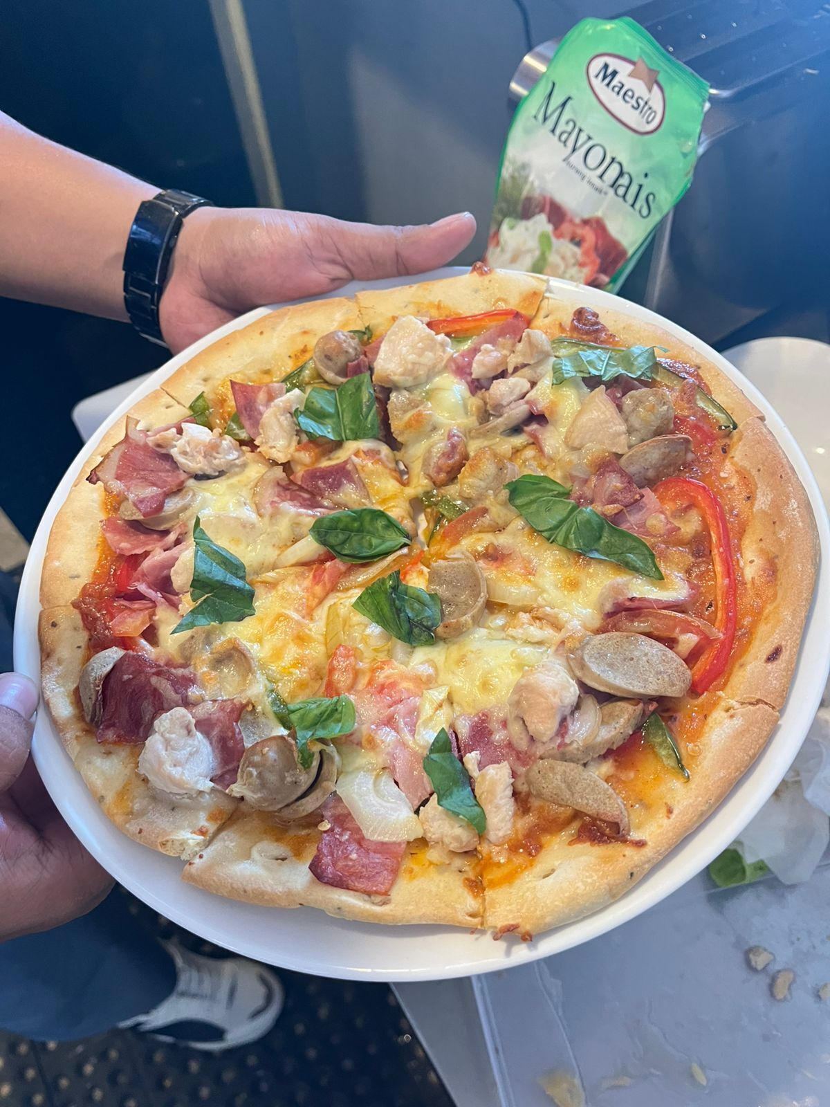 Une pizza garnie de divers ingrédients, tenue par une personne.