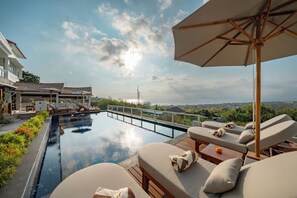 A rooftop infinity pool with lounge chairs and an umbrella, overlooking a scenic view.
