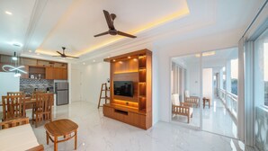 Una sala de estar moderna con mueble de entretenimiento de madera, un comedor con muebles de madera y una cocina al fondo.