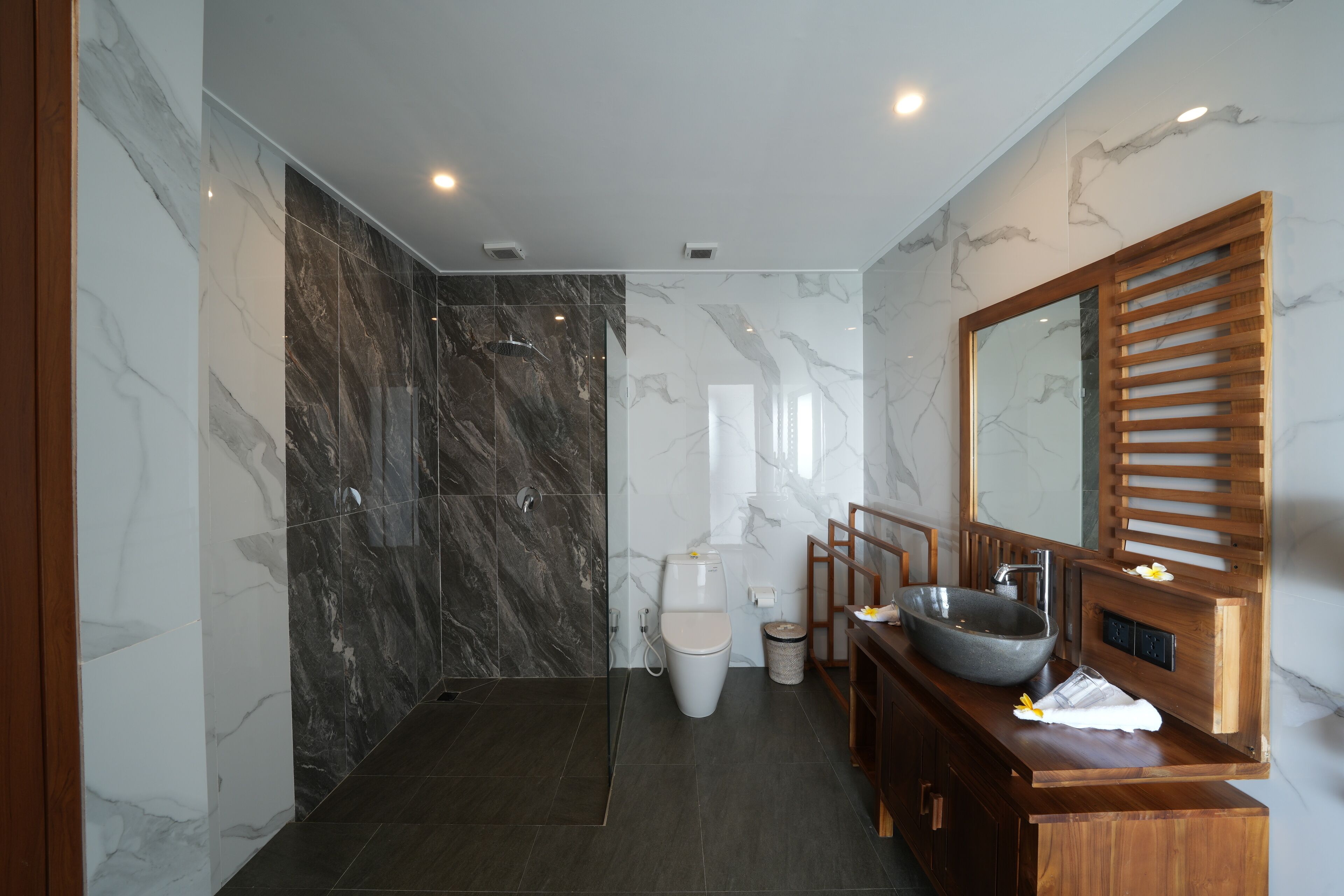 Un baño moderno con un espejo grande, un tocador de madera y una zona de ducha de mármol.