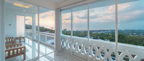 A spacious balcony with large windows offering a view of a cityscape and greenery.