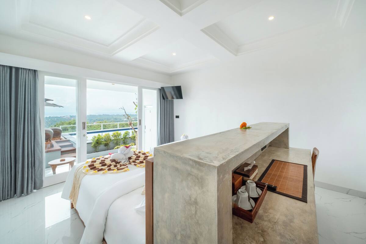 Ein modernes Hotelzimmer mit einem großen Bett, einem Schreibtisch aus Beton und Blick ins Freie.