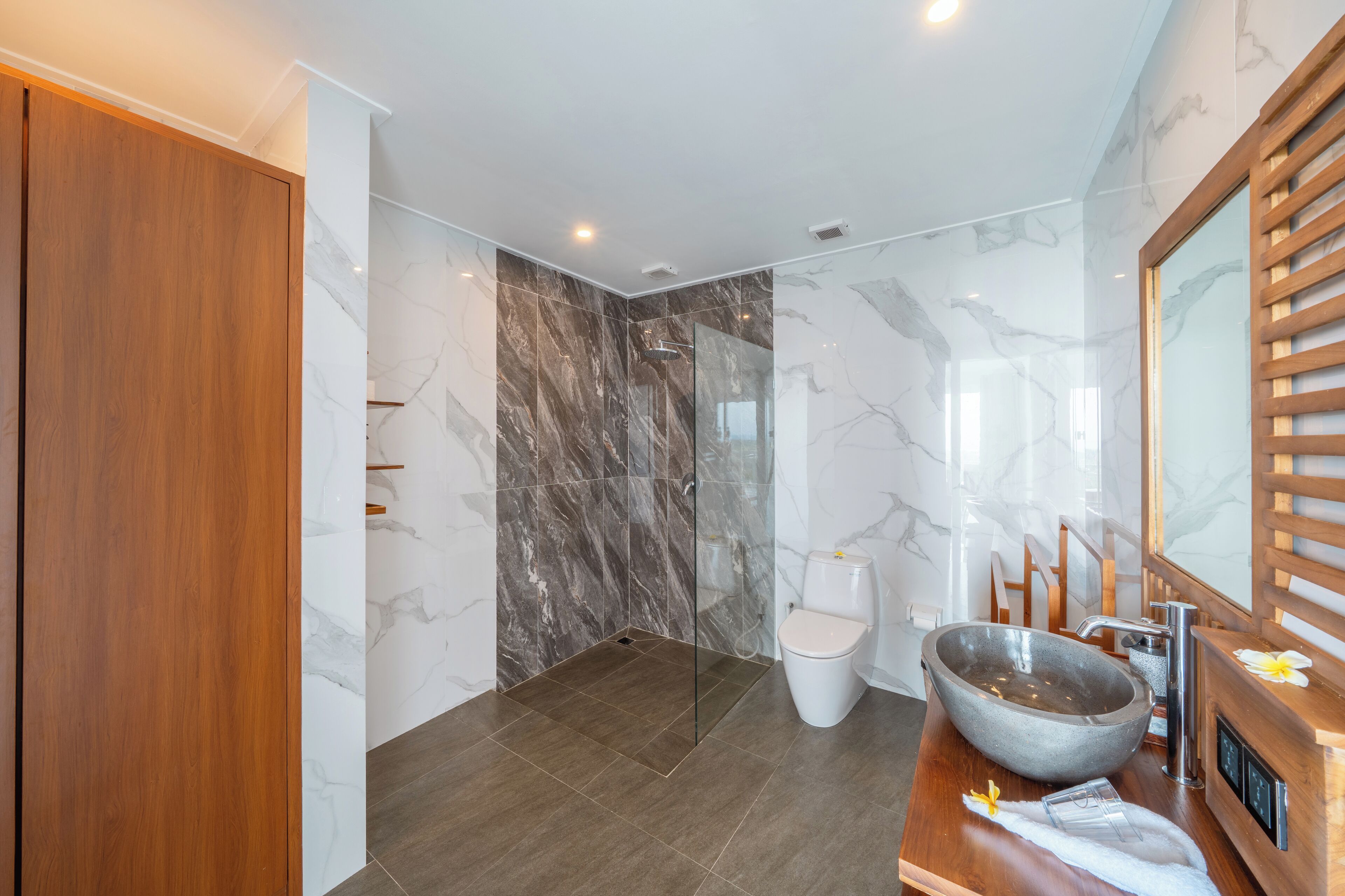 Een moderne badkamer met een houten wastafelmeubel, een grote waskom, een toilet en een douchecabine van glas.