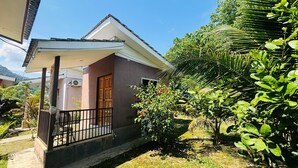 Una casa residencial con balcón, puerta de madera y jardín con diversas plantas.
