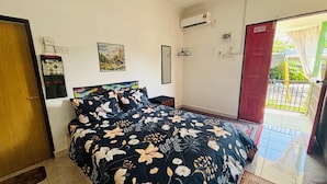 Un dormitorio con cama, mesita de noche, aire acondicionado instalado en la pared, una puerta y una ventana con vistas al exterior.