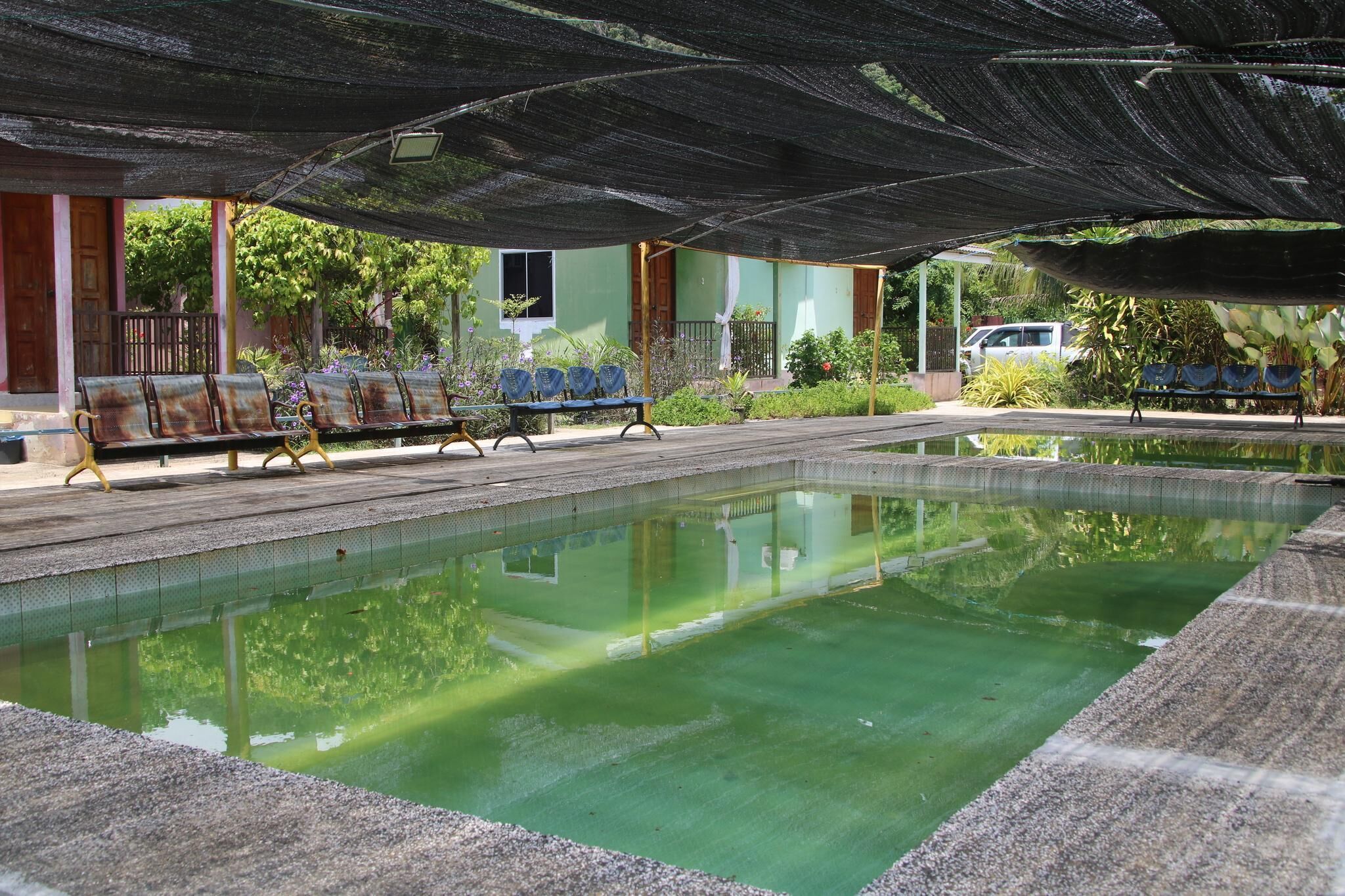 Zona de piscina con un área de estar cubierta y un edificio al fondo.
