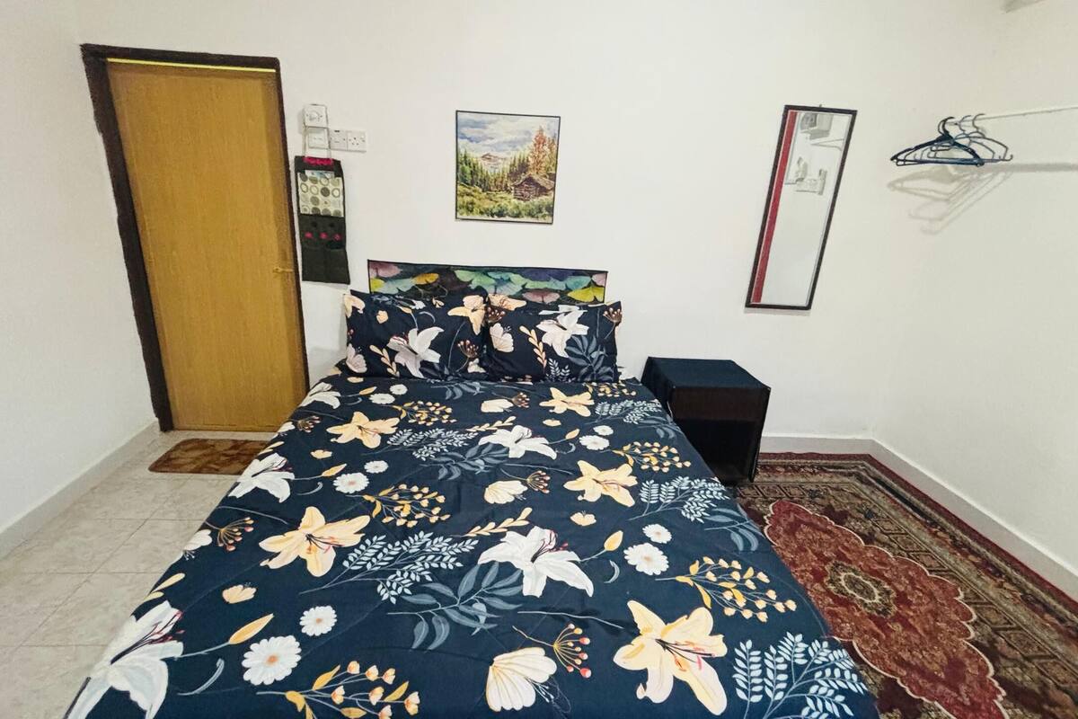 A bedroom with a bed, a nightstand, a rug, a door, and a wall with a picture and a coat rack.