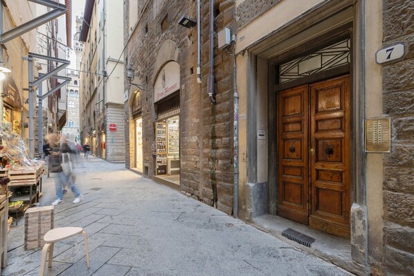 A narrow street with stone buildings, wooden doors, and a visible shop on the left.