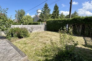 A grassy yard with a wooden fence, a white building with a tower, and trees. - 🌿 Hozanna - Chic & charming interlude in Le Crotoy 🌿 (LE CROTOY)
