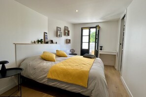A bedroom with a bed, a bedside table, a chair, a window, and a door.