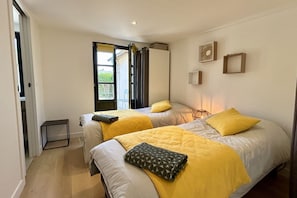 A bedroom with two beds, a small table, and a window with curtains.