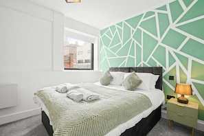 Quarto de hotel moderno com uma cama, uma janela, uma parede geométrica verde e um abajur.