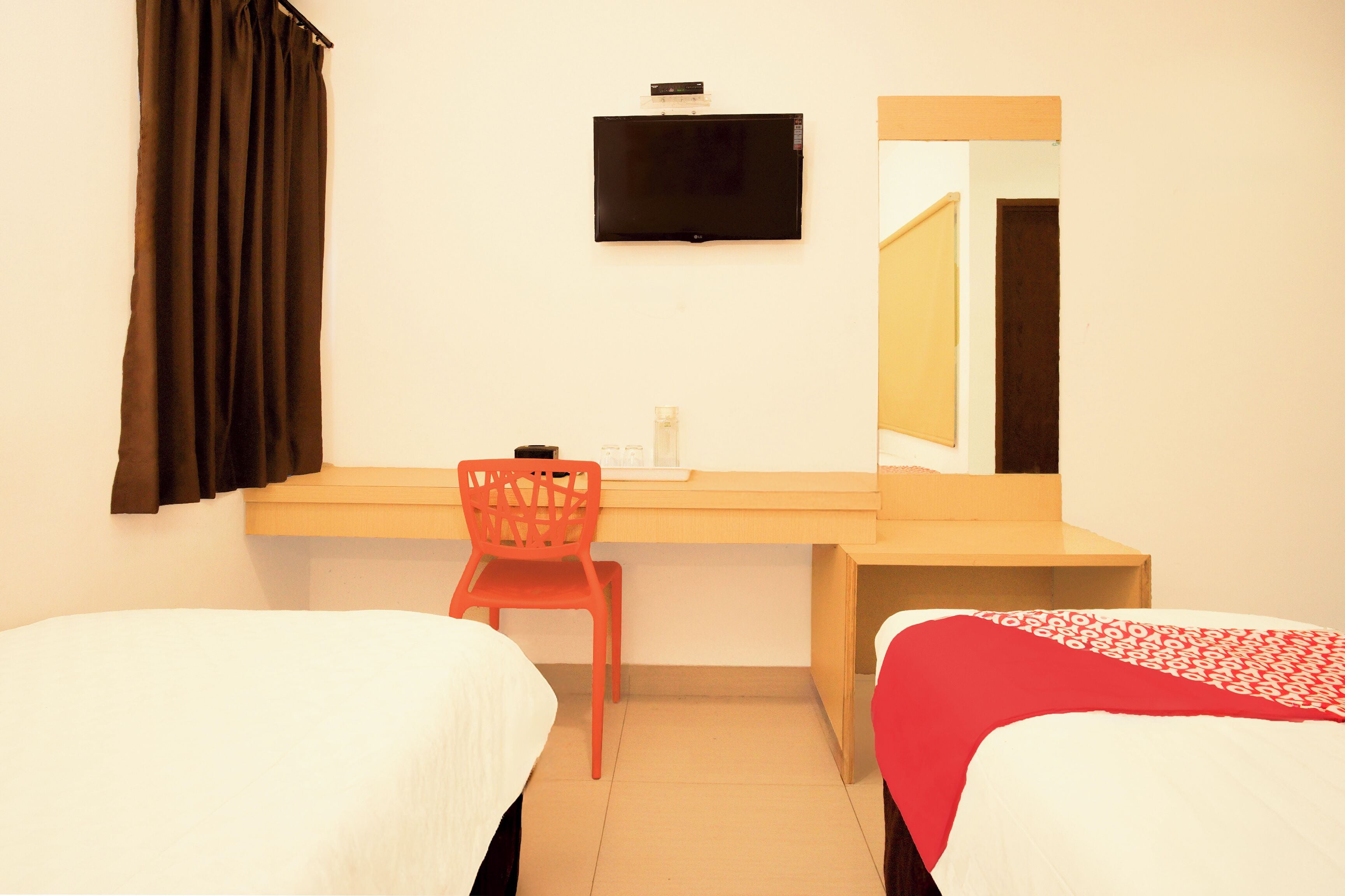 A hotel room with two beds, a desk, a chair, a TV, and a mirror.
