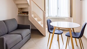 A modern living space with a staircase, a dining area with a table and chairs, a sofa, and a TV mounted on the wall.