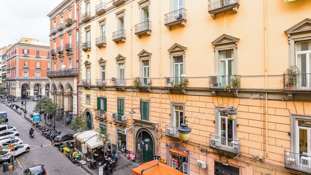 A street view with a row of buildings, some with balconies and shops on the ground floor.