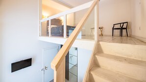 A staircase with a wooden handrail leading to a second-floor room with a bed and a window.