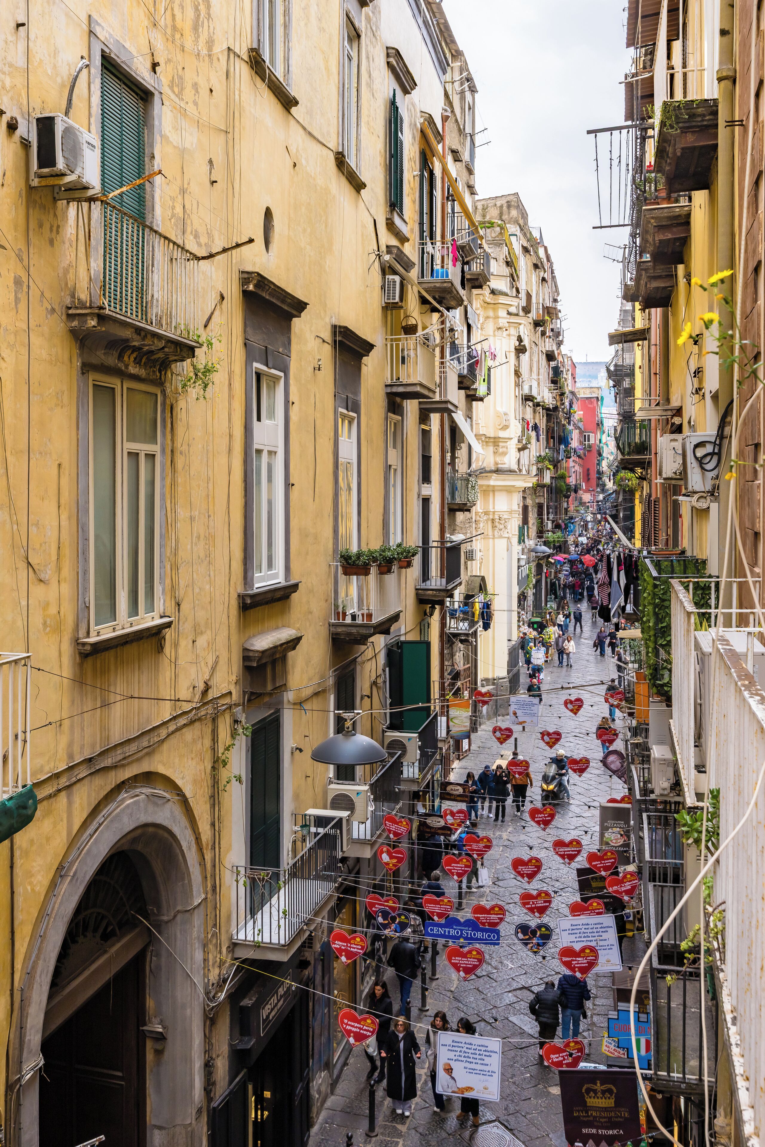 A narrow street lined with old buildings, some with balconies and air conditioning units.