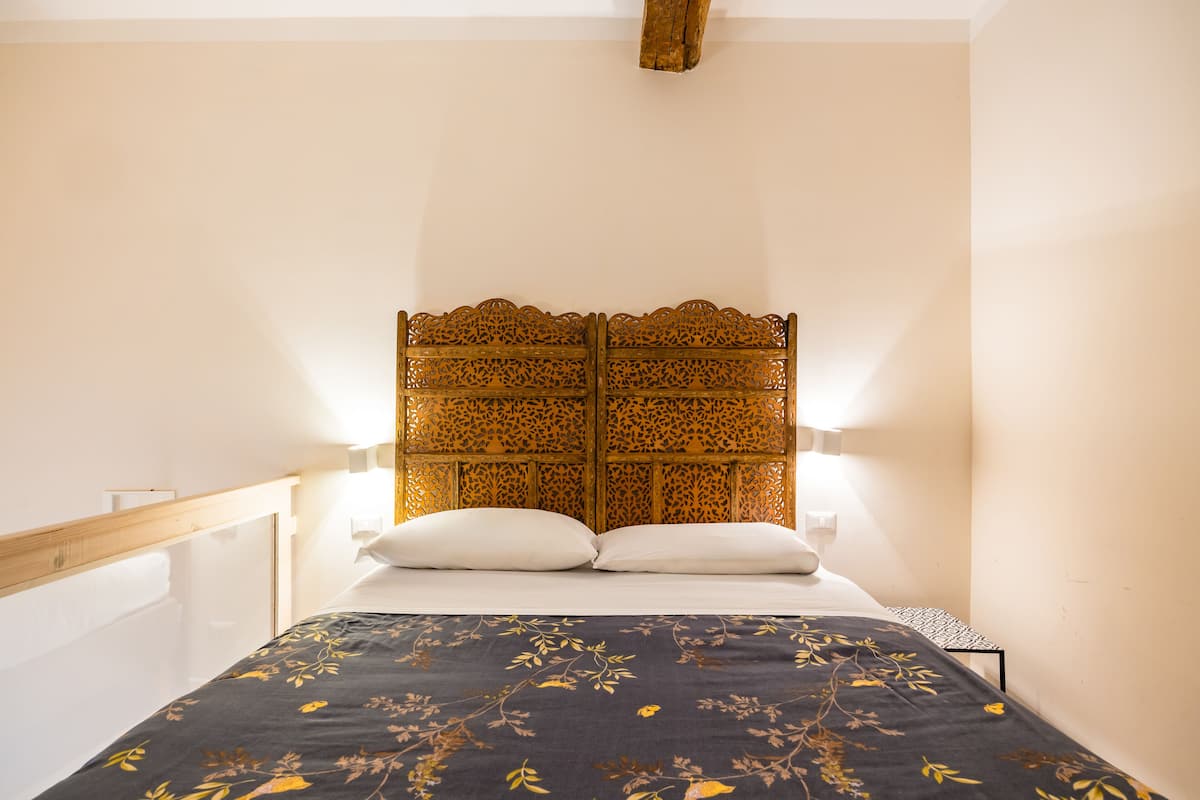 A bed with a dark floral bedspread, a wooden headboard with intricate carvings, and two bedside lamps.