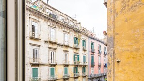 A view from a window overlooking a street with buildings, a yellow wall, and a metal railing.