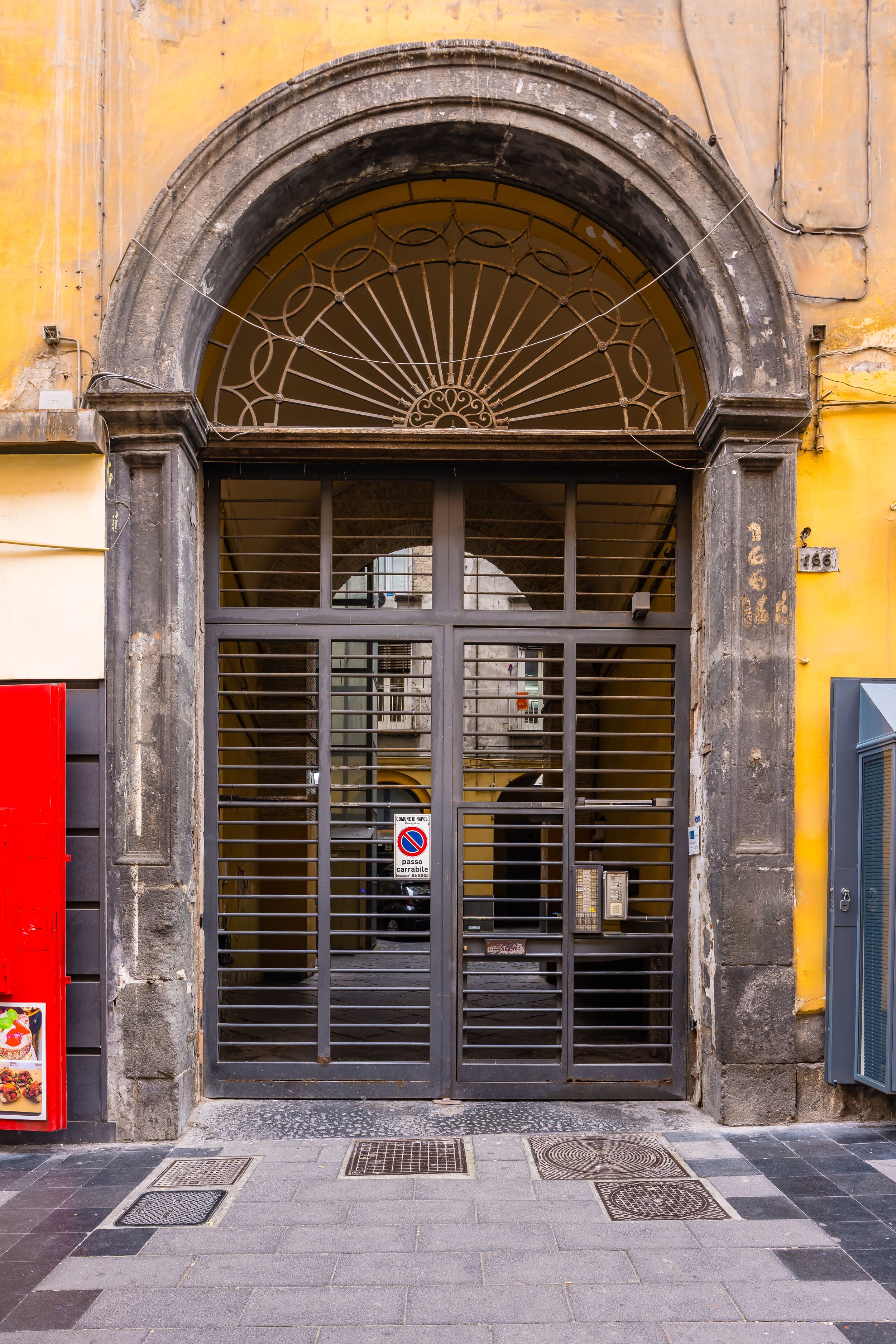 A building entrance with a large arched door, a barred window, and a "No Parking" sign.