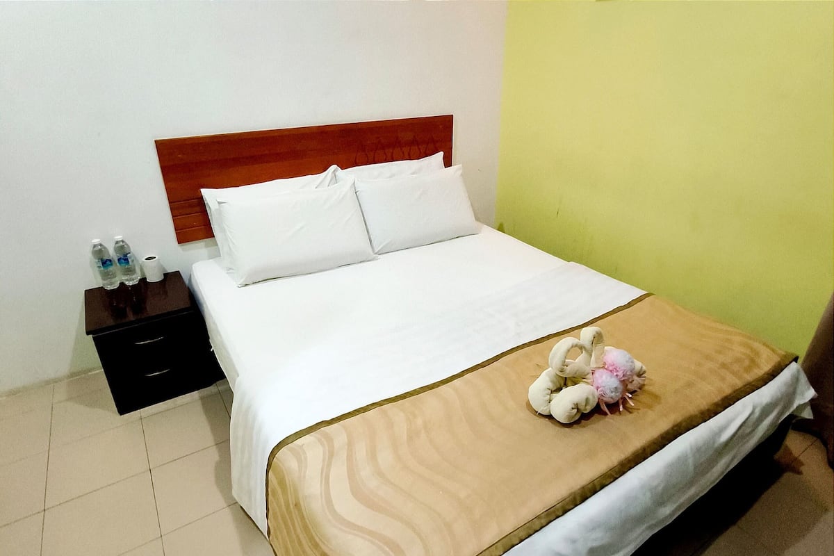 A neatly made bed with a wooden headboard, a bedside table with bottled water, and a plush toy on the bed.
