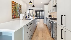 Una cocina moderna con armarios blancos, una isla central, iluminación colgante y vistas al comedor.