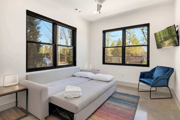 A modern room with a sofa, a chair, a TV, and large windows.