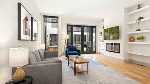 A modern living room with a sofa, a blue armchair, a coffee table, a fireplace, and a TV.