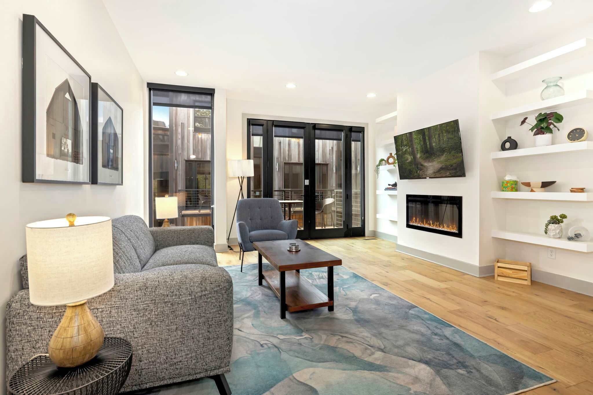 A modern living room with a sofa, armchair, coffee table, fireplace, and artwork on the wall.