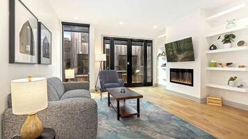 A modern living room with a sofa, armchair, coffee table, fireplace, and artwork on the wall.