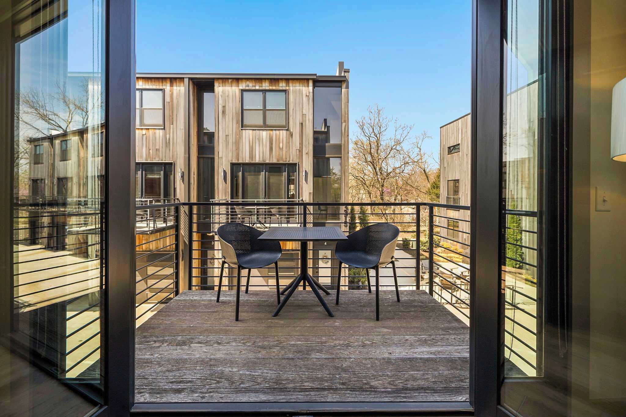 A balcony with a table and chairs, a wooden floor, and a view of a modern building.