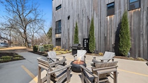 Un edificio moderno con fachada de madera, mobiliario exterior con sillas y una chimenea, además de una parrilla de barbacoa.