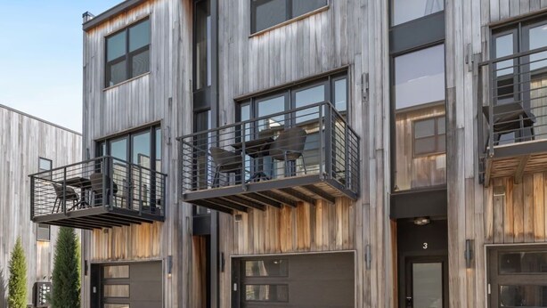 Un edificio moderno de varios pisos, con amplias ventanas, balcones y entrada de garaje.