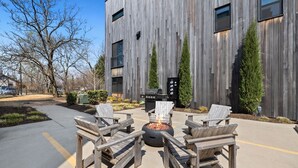 A modern building with a wooden facade, outdoor seating with chairs and a fire pit, and a barbecue grill. - Scout - Trailhead Mews - Optional BlakeSt Access (Bentonville)
