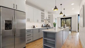Une cuisine moderne dotée d’appareils électroménagers en acier inoxydable, de meubles blancs et d’un îlot central.