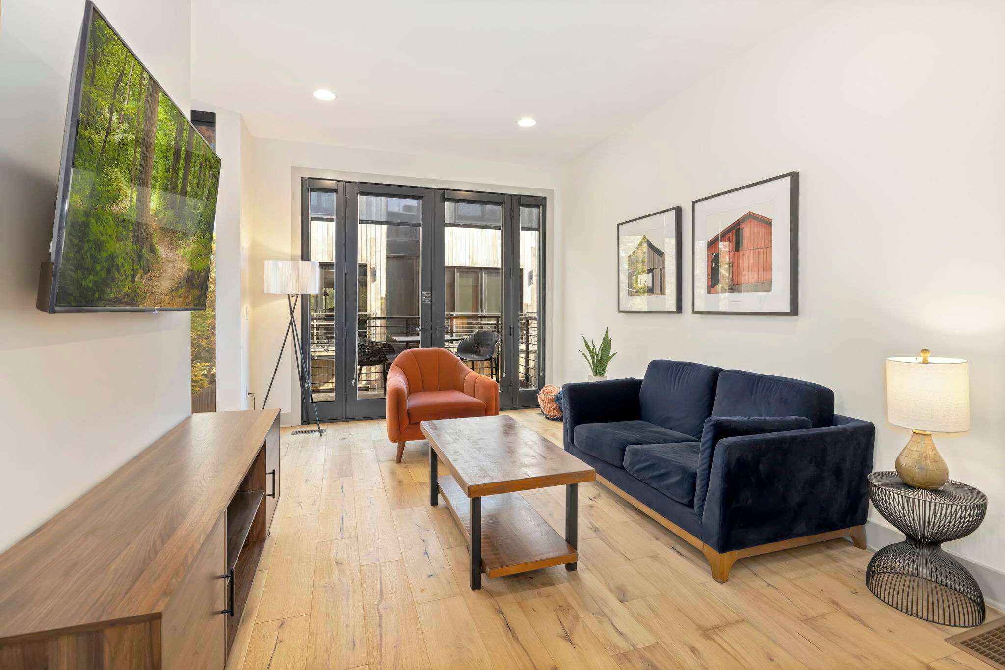Ein modernes Wohnzimmer mit einer Couch, einem Couchtisch, einem Fernseher und einer Schiebetür zu einem Balkon.