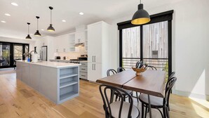 A modern kitchen with white cabinets, a wooden dining table, and pendant lighting. - Venture - Trailhead Mews - Optional BlakeSt Access (Bentonville)