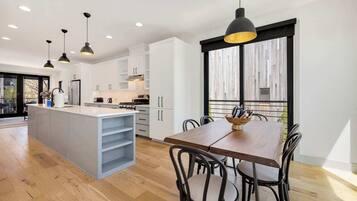 A modern kitchen with white cabinets, a wooden dining table, and pendant lighting.