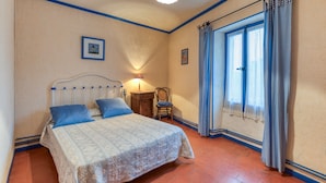 A bedroom with a bed, a chair, a small table, and a window with curtains.